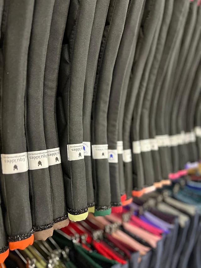 Tapis de selle Equ'Idées suspendus en rayon sur le stand d'Equita, bords de couleurs variées