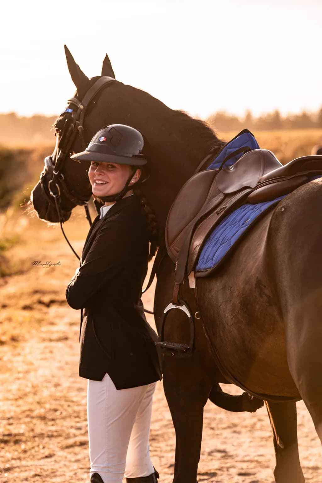 Cavalière debout près d'un cheval bai foncé sellé, tapis de selle bleu roi