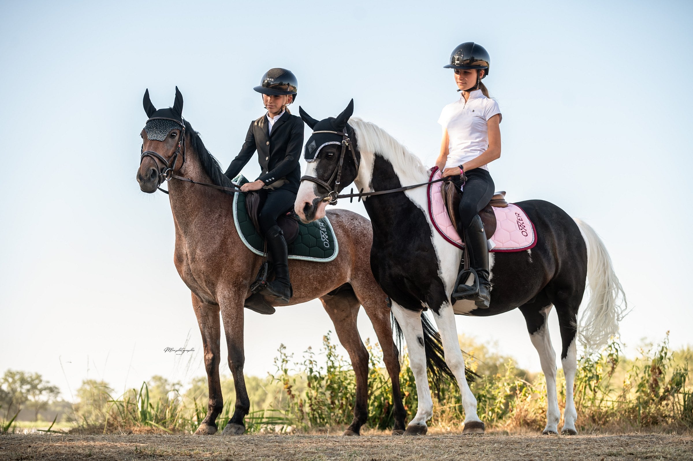 Deux cavalières côte à côte en extérieur, tapis de selle rose pâle et vert