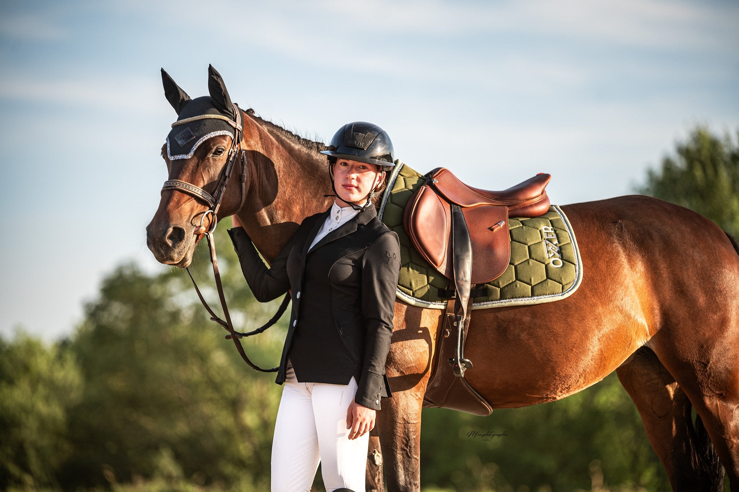 Cavalière debout près d'un cheval bai sellé, tapis de selle vert kaki