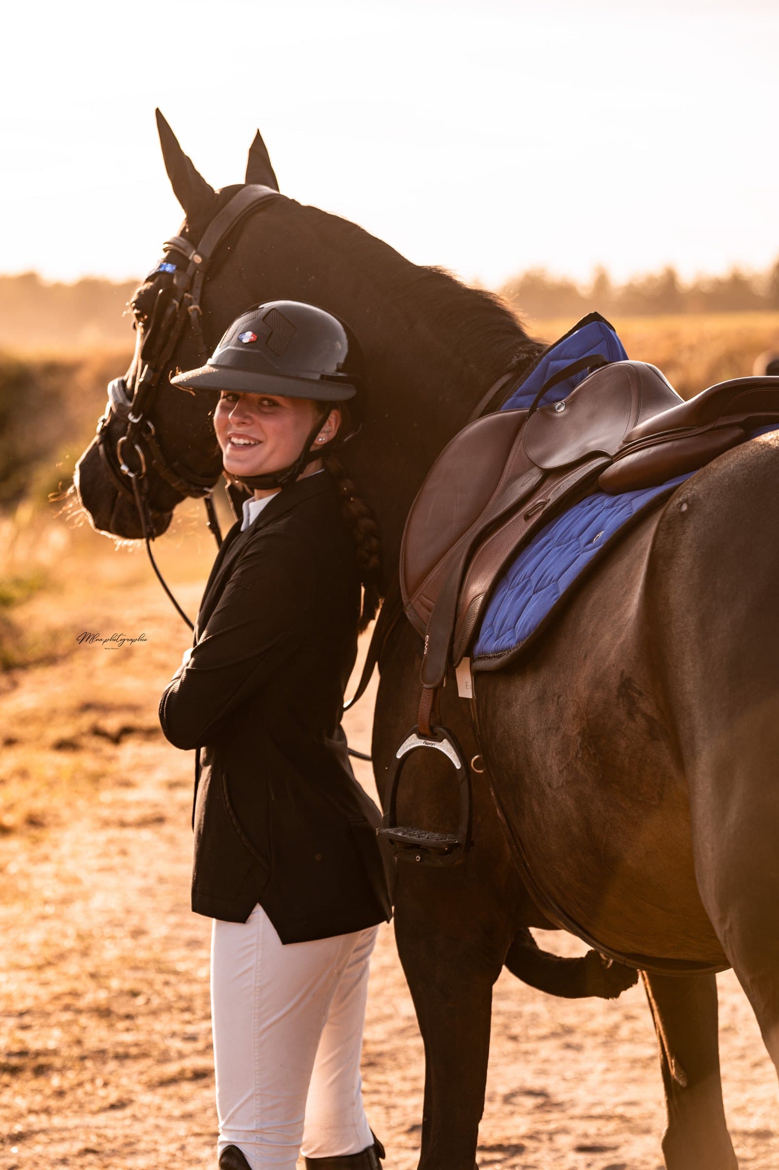 Cavalière debout près d'un cheval bai foncé sellé, tapis de selle bleu roi