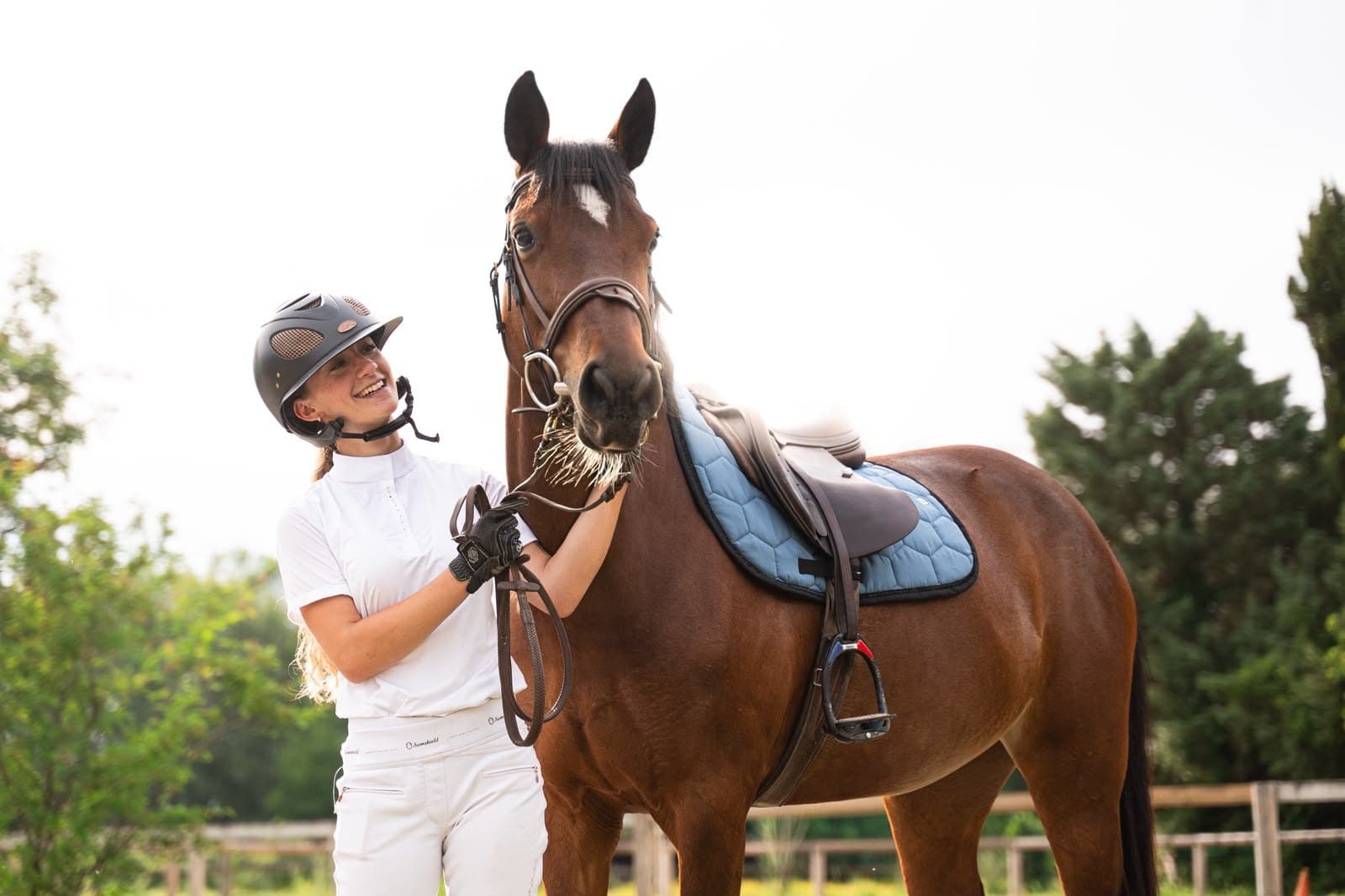 Cavalière tenant un cheval bai sellé, tapis de selle bleu glacier